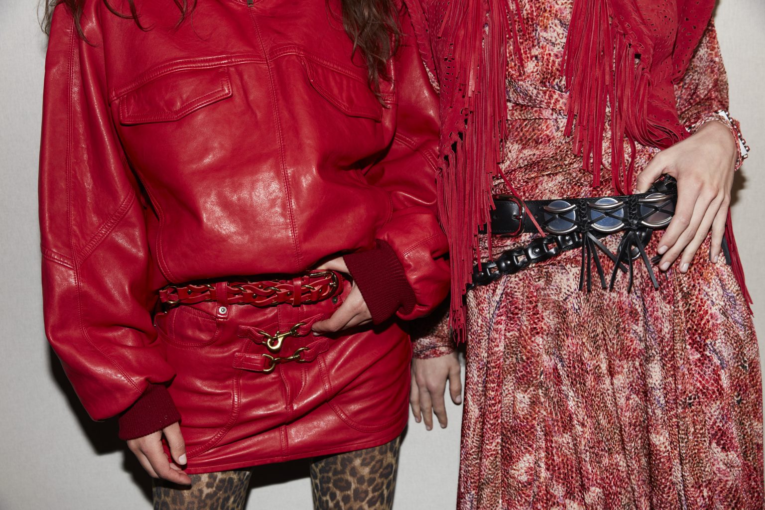 Two female midsections, one wearing a red patterned dress and red fringed scarf, the other in a red leather jacket and miniskirt.