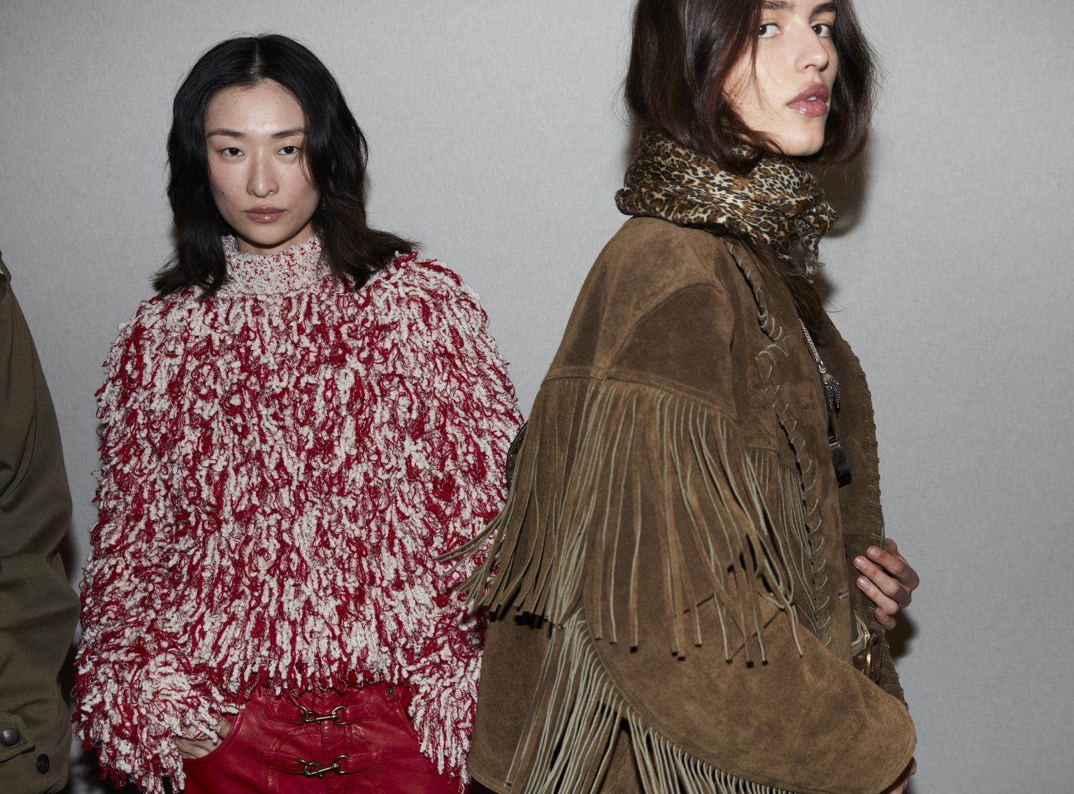 Two female models, one wearing a brown suede fringed jacket and leopard-printed scarf, the other in a shaggy red and white oversized sweater.