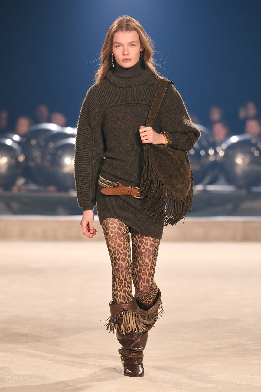 Image of female model on catwalk wearing a chocolate brown chunky-knit sweater dress with a low-slung belt, leopard tights and brown fringed boots.
