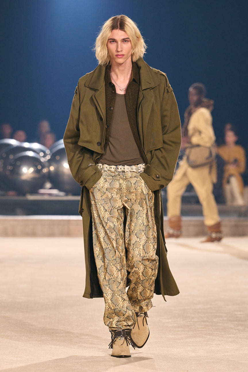 Image of model on catwalk wearing an oversized khaki trench and brown tee, baggy tan snakeskin-printed pants and tan pointed-toe shoes.