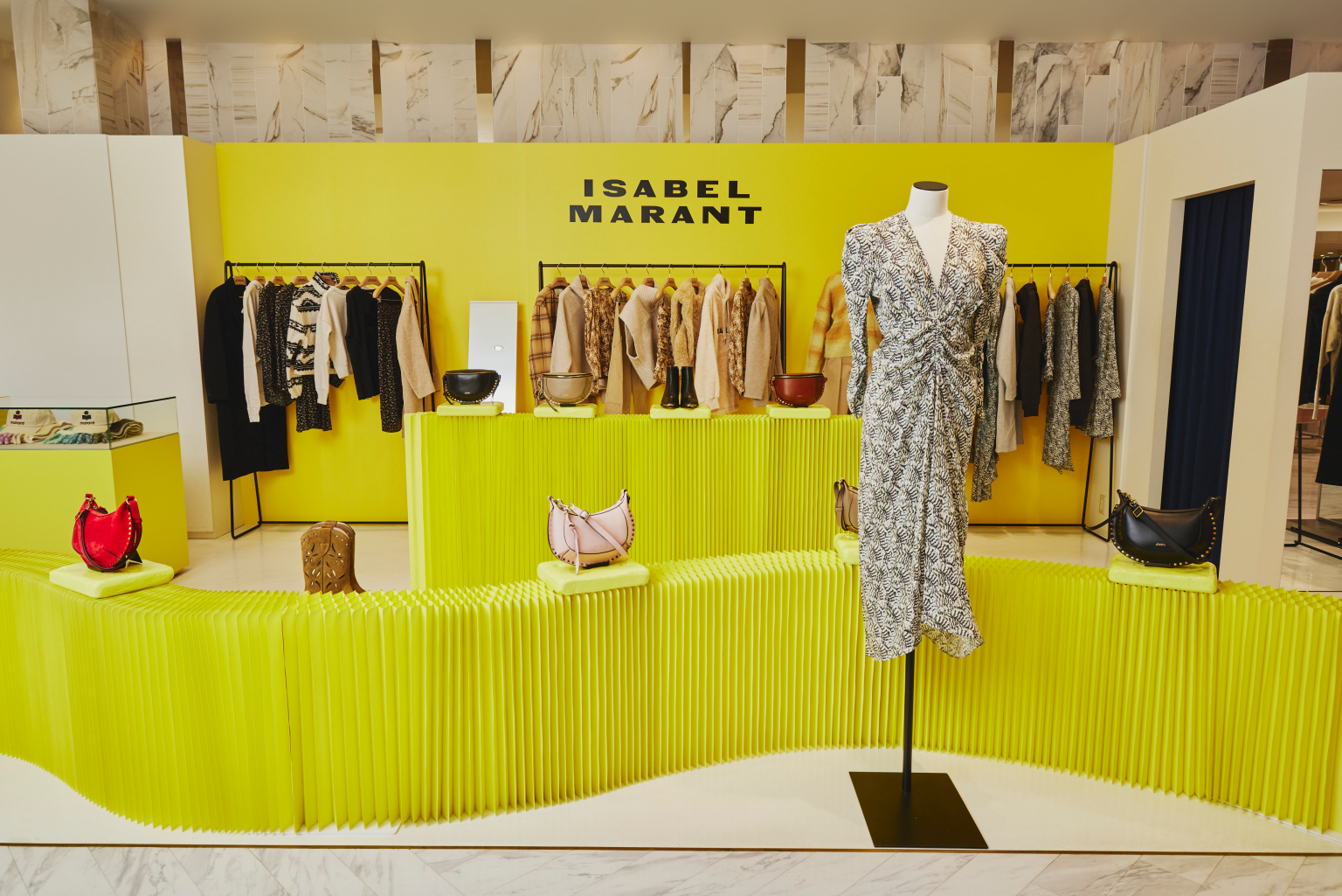 Image of yellow display area featuring the Isabel Marant clothing collection with a ruched and printed midi dress displayed in the foreground.